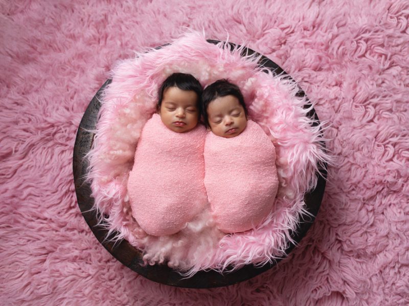 twin-baby-girls-wrapped-in-pink-wraps-sleeping-side-by-side-in-a-wooden-bowl