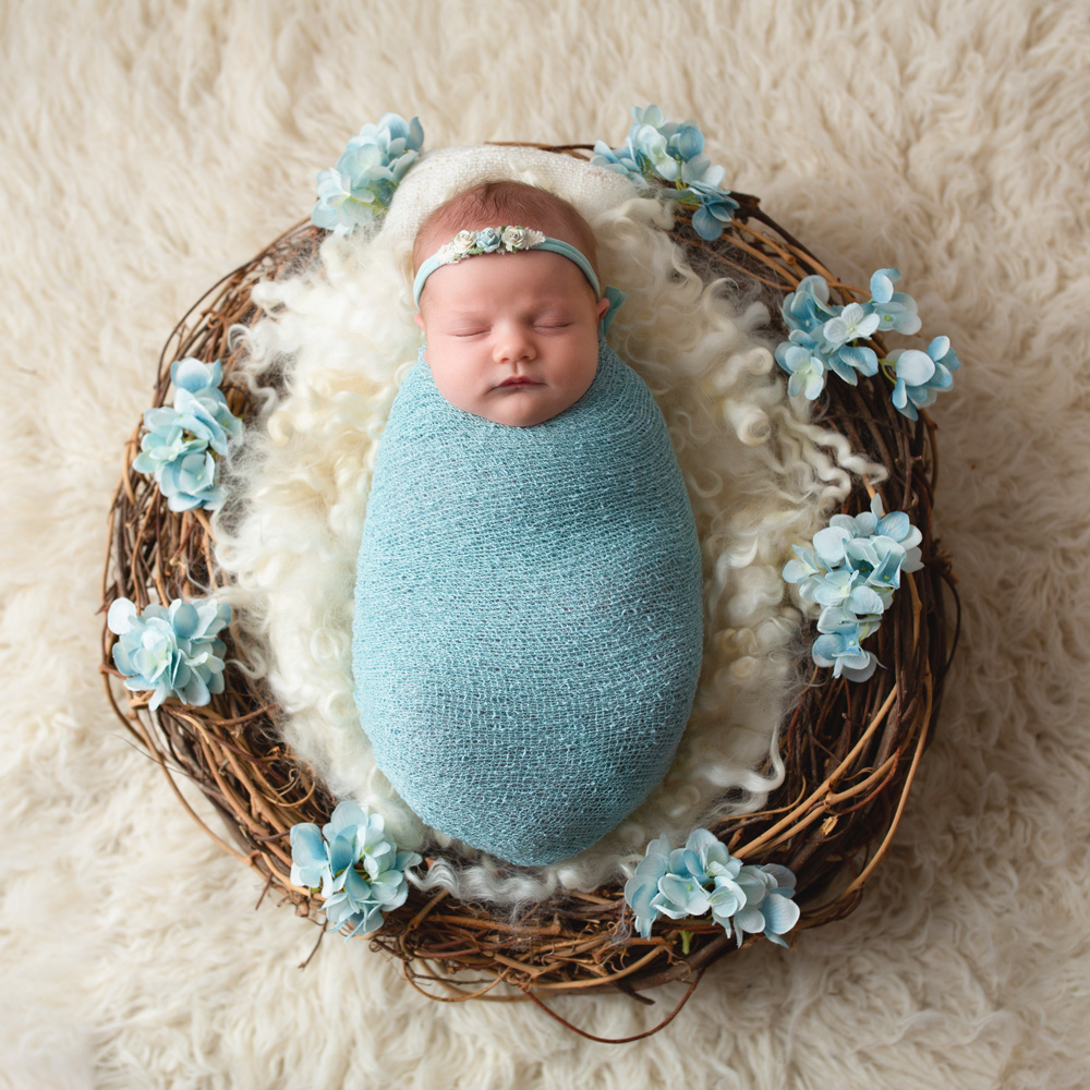 baby-girl-laying-asleep-in-a-nest-with blue-flowers